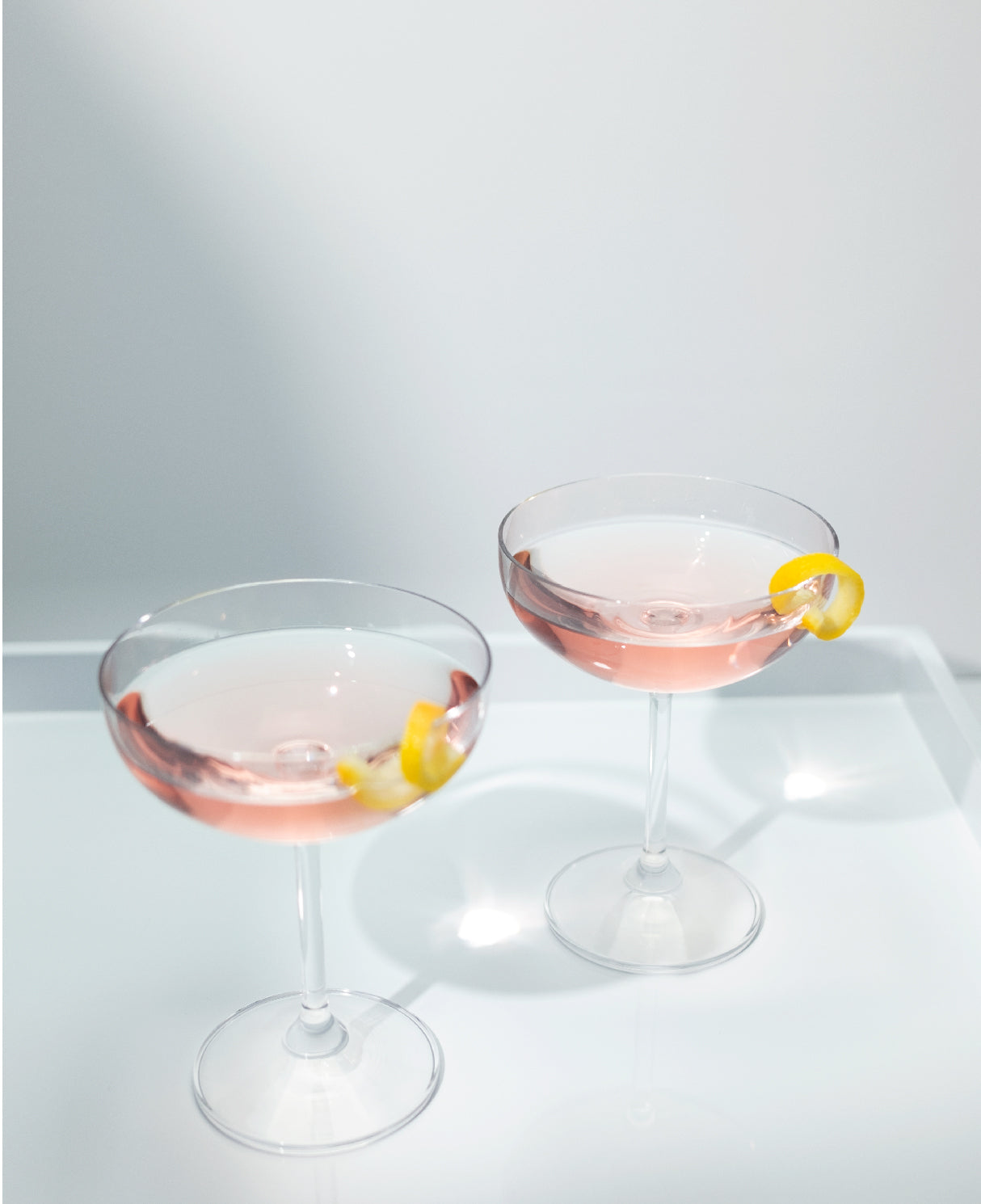 Two Cosmopolitan cocktails in coupe glasses, garnished with a lemon twist.