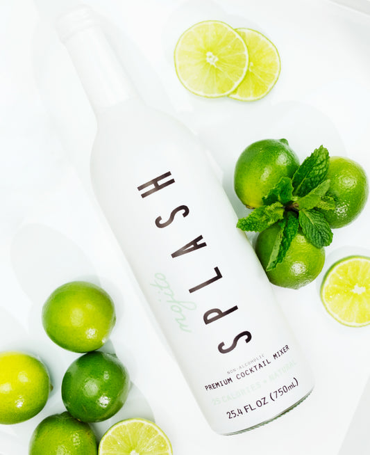 Splash Mixers Mojito bottle next to limes and sprig of mint.
